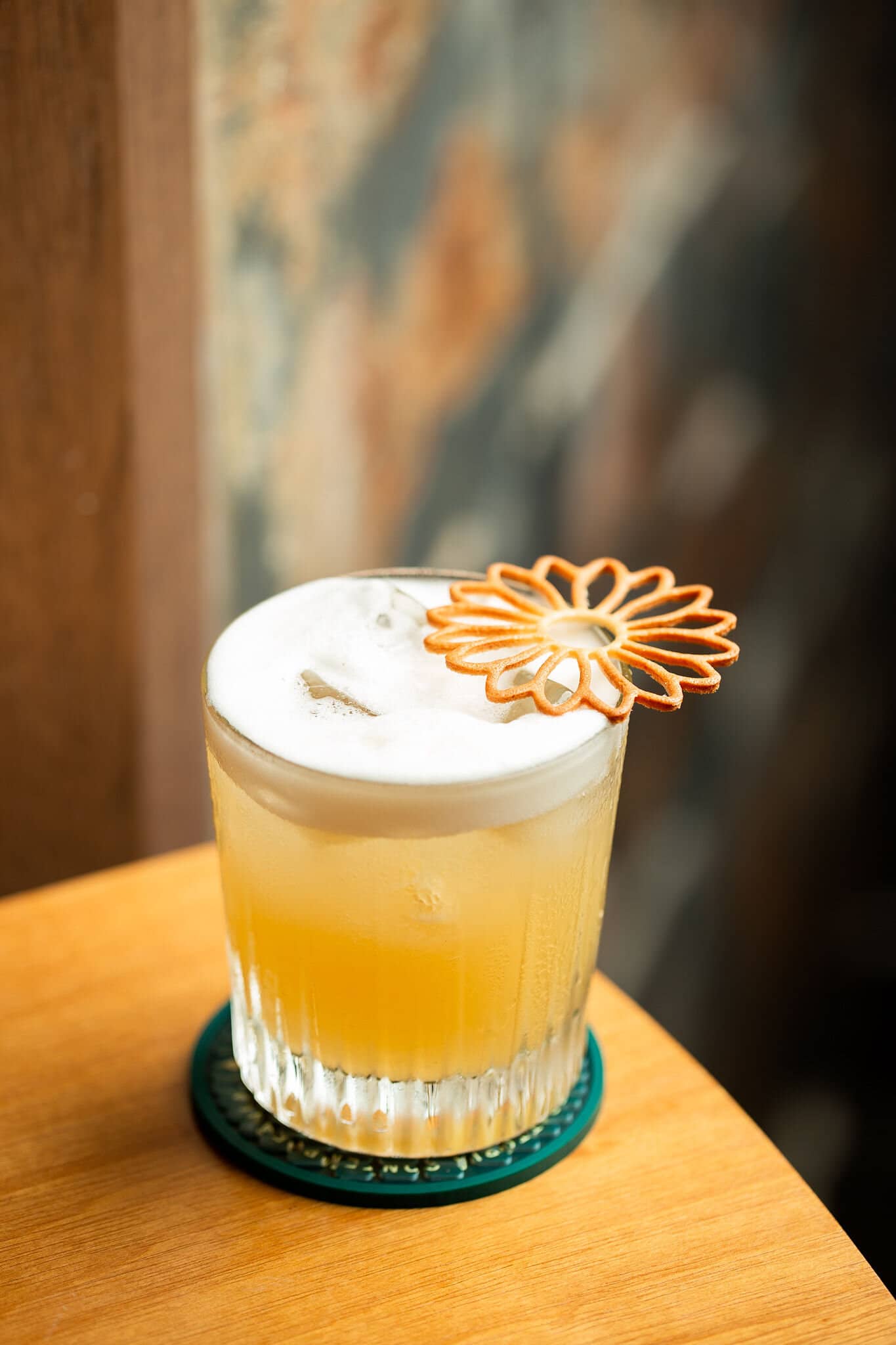 Drink with light foam in a short glass, with a caramelised sugar flower, on a wooden table.