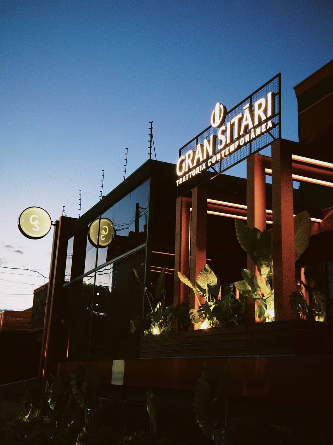 Fachada do Gran Sitári ao entardecer, com o letreiro iluminado e folhagens na varanda.