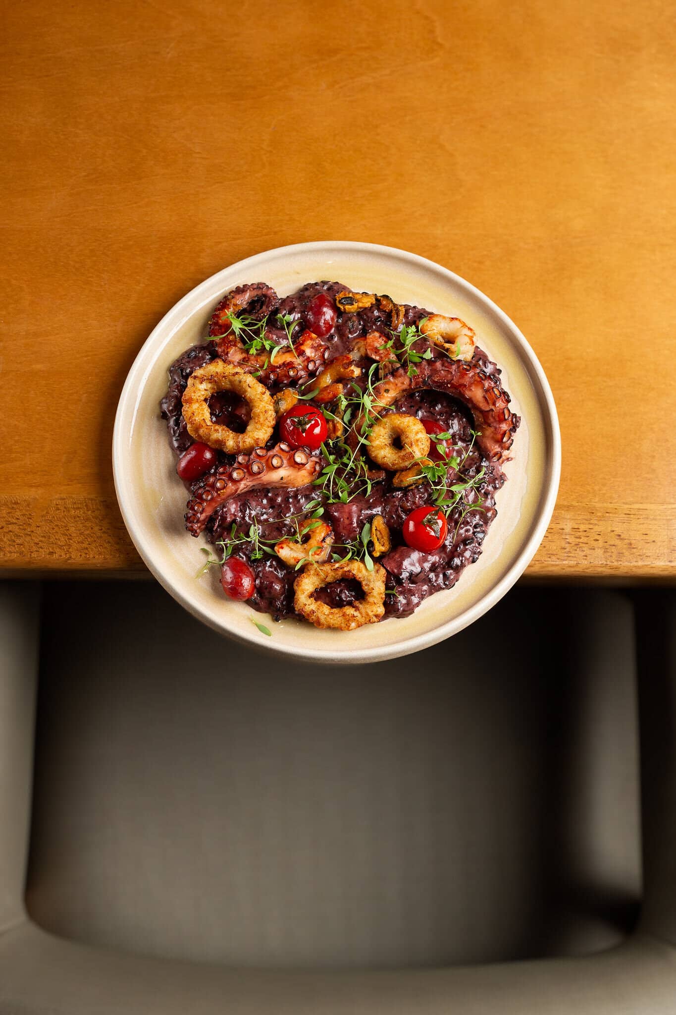 Grilled octopus with crispy rings and cherry tomatoes on a light plate, on a wooden table.