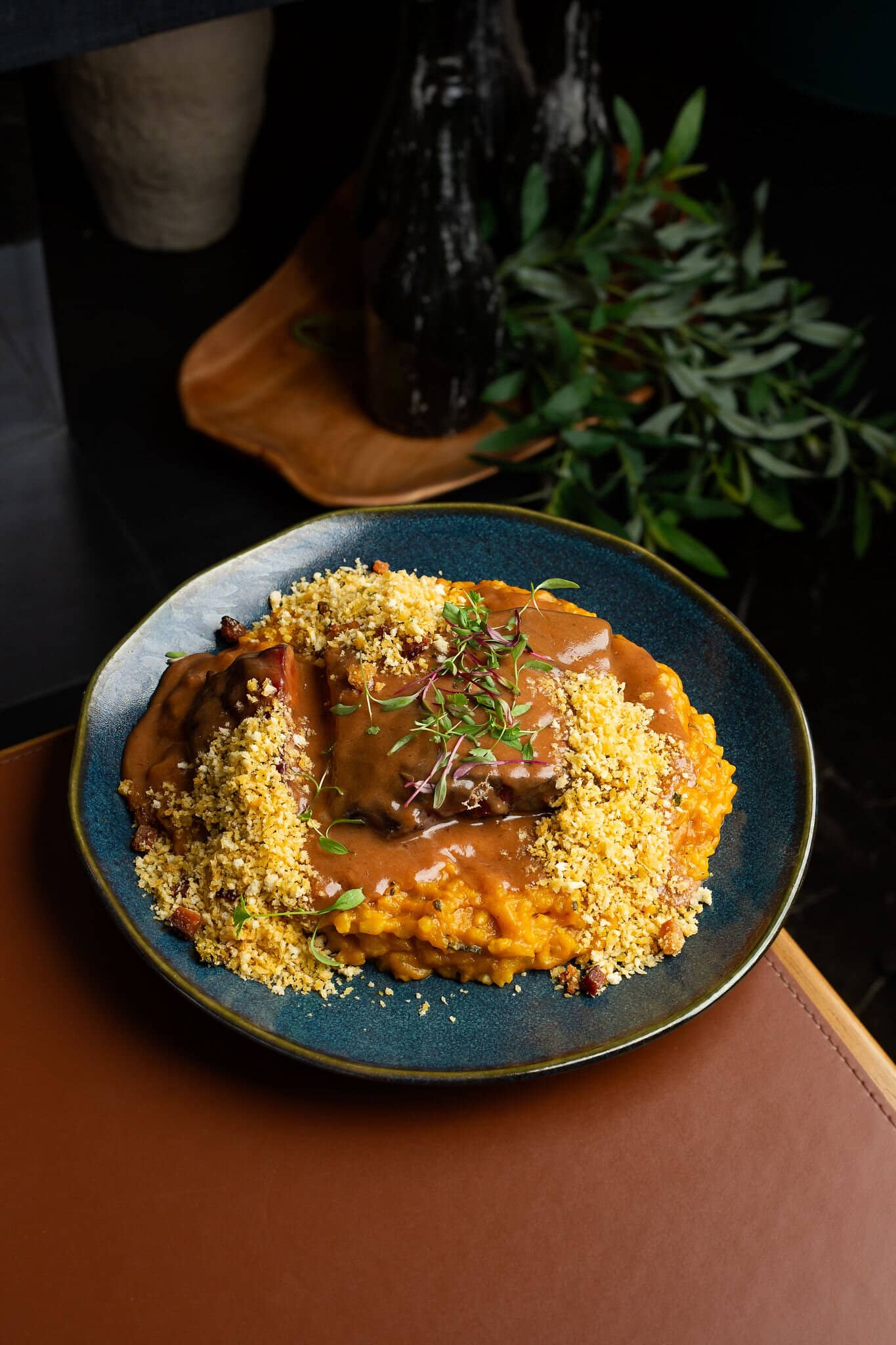 Kabocha squash risotto with pork ribs and farofa, in a blue plate on a wooden table.