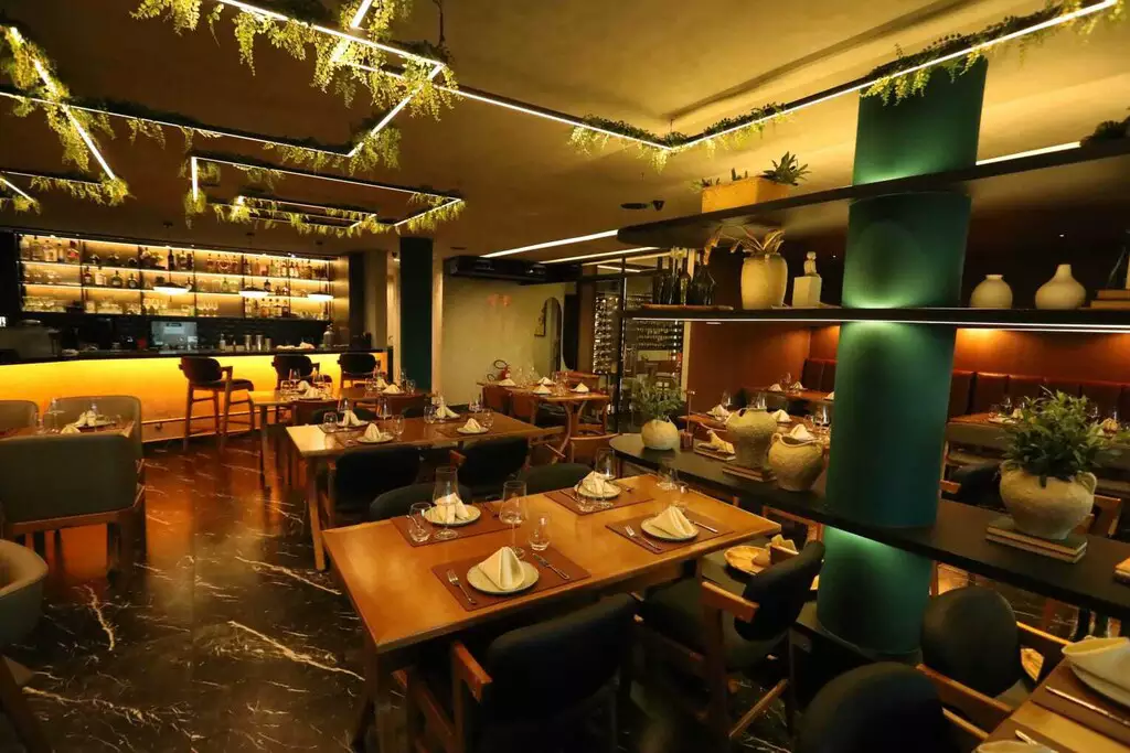 Balcão do bar do Gran Sitári, com a prateleira de garrafas iluminada e banquetas de madeira.