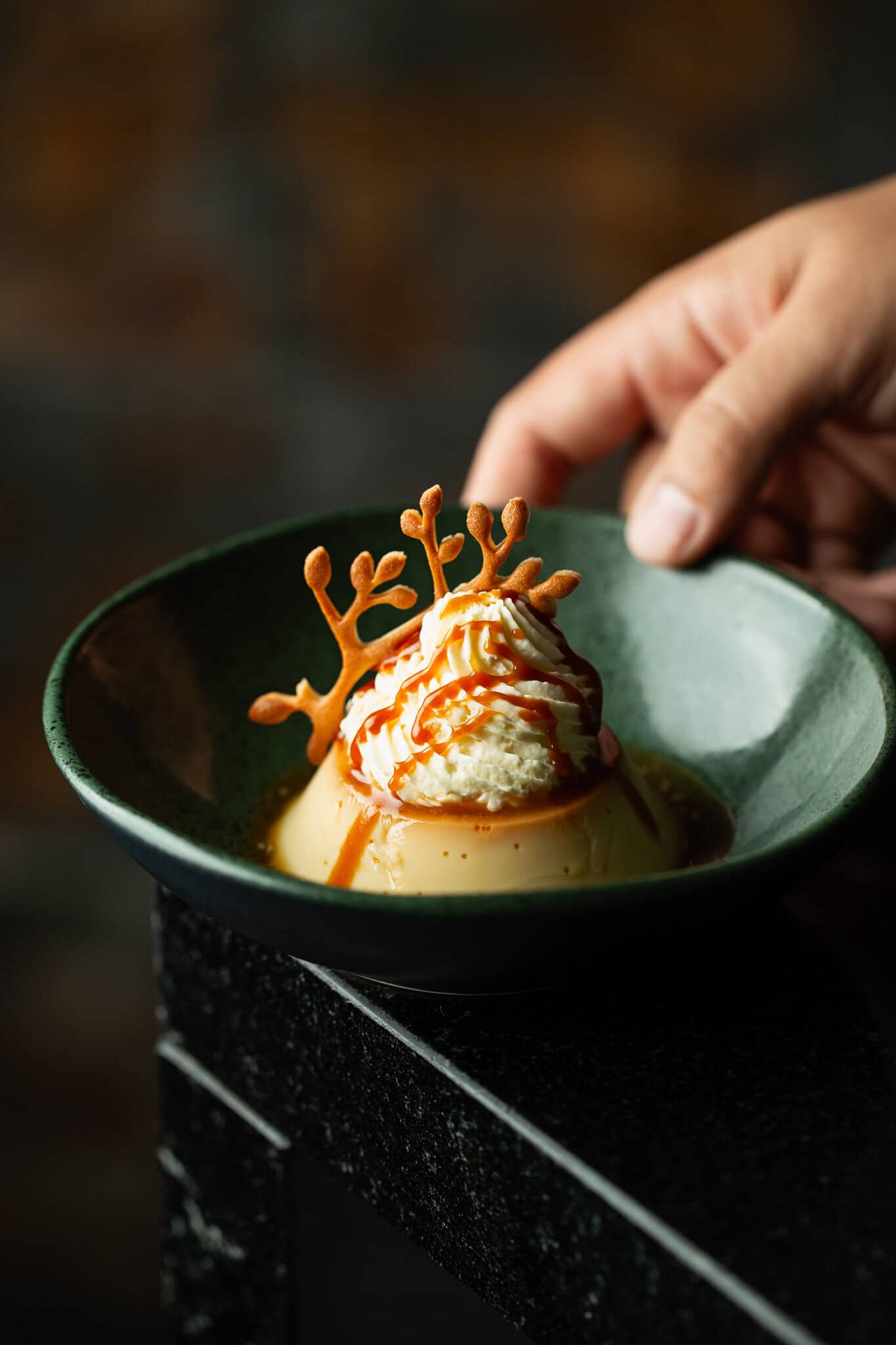 Dessert with cream and caramel sauce and a golden tuile, on a dark green plate.