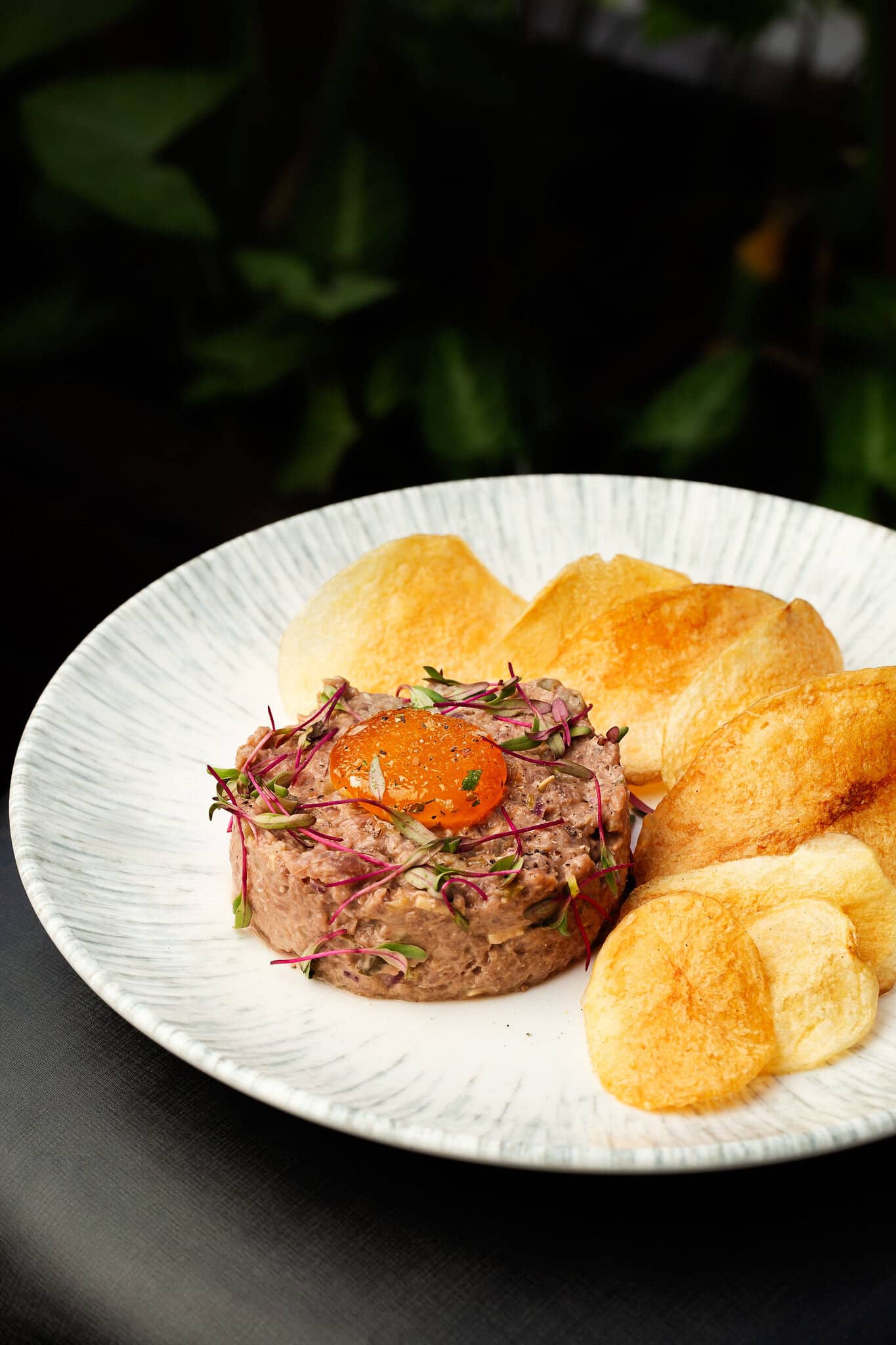 Beef tartare with cured egg yolk and potato chips on a white striped plate.